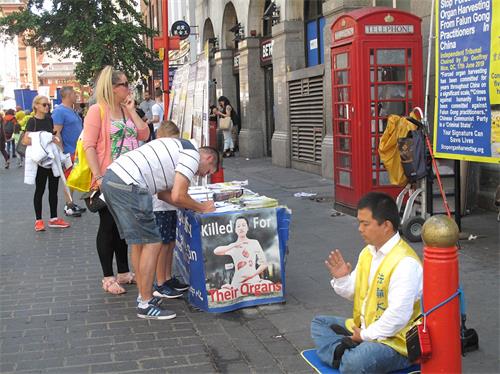 '图2:在伦敦唐人街,“反迫害二十周年”游行队伍让一对英国夫妇第一次看到法轮功真相,他们马上来到法轮功学员在唐人街讲真相点继续了解真相,并签名支持制止迫害。'