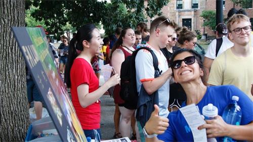 '图6:一位了解了大法的学生开心的在大法摊位前留影'