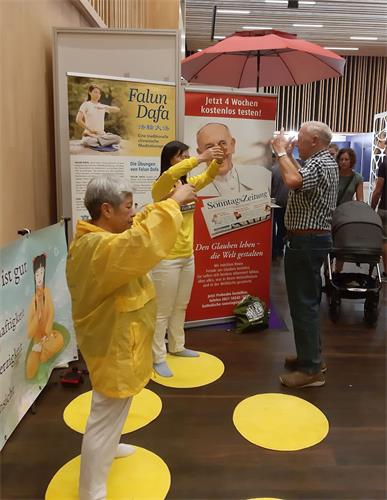 '图1~2:法轮功学员在健康展上示范功法时,不断有参观者留步,并尝试学功。'