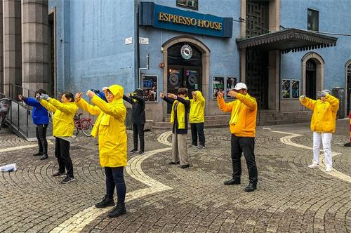 '图1:法轮功学员在音乐厅旁举办讲真相活动。学员们在雨中展示功法。'