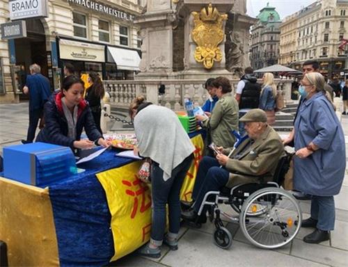 '图2:格拉本大街瘟疫柱前的展台前民众排队签名反迫害'