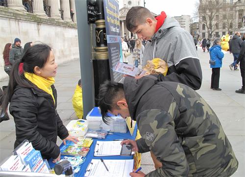 图6:二零二零年三月七日,在特拉法加广场,两个大学生丹尼斯(Denis)和马里斯彭(Marispen)签名支持法轮功反迫害。