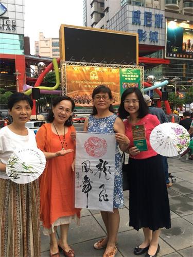 '图2:刘明辉的妻子(左二)是书法家,在神韵推广活动中,现场挥毫的作品致赠给购票的民众。'