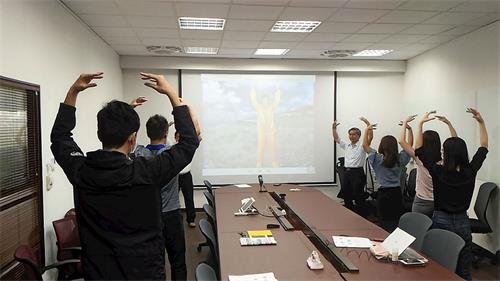 '图1:在公司会议室里举办的法轮功九天学法班,新学员们跟着教功录像带炼功。'