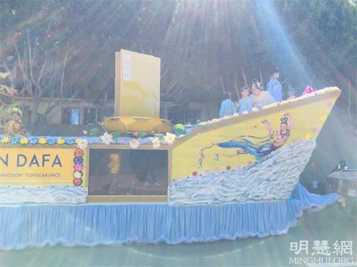 图:在游行队伍整装待发时,学员照到彩色的光芒照射着承载《转法轮》的花车。