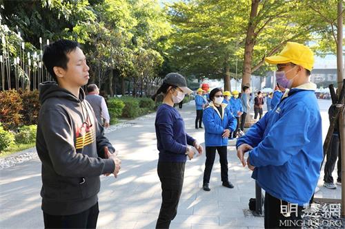 '图13:卢女士(中)正在活动现场旁学炼法轮功。'