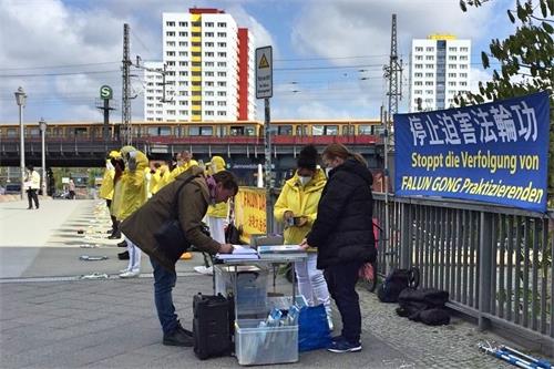 '图2:二零二一年四月二十三日,路过的民众得知中共活摘法轮功学员器官的罪行后,在学员的请愿书上签字,谴责中共暴行。'