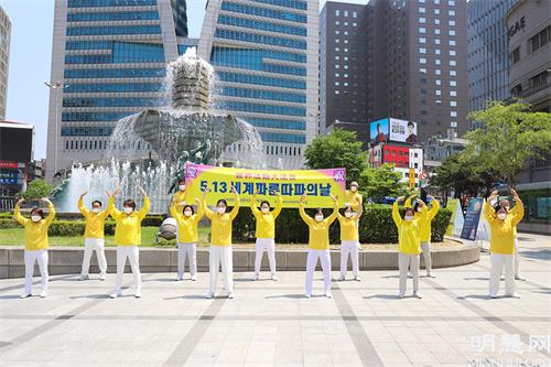 图2:5月13日,部分首尔西部和中部的法轮功学员们在首尔市中心新世界百货店附近的大型喷泉前举行了集体炼功、派发传单等洪法活动。图为他们在集体炼功的场面。