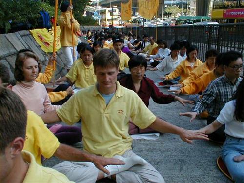 '图3:一九九九年十二月十一日下午一点至三点,在新华社斜对面,法轮功学员举行了大型集体炼功。慈悲祥和的场面与烦闹沸腾的市容形成鲜明的对照,吸引了众多的路人驻足观看,过往的大巴士中不少人也为之喝彩。图为当时西蒙参加炼功的场景。'