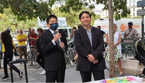 '图9:驻法国台北代表处的国会组秘书程瑞安先生(左)在集会上讲话'