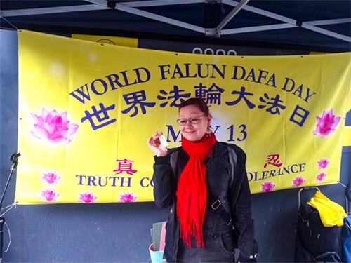 图8:残疾人指导教师T. Pyy女士手拿小莲花,在“世界法轮大法日”横幅前拍照留影