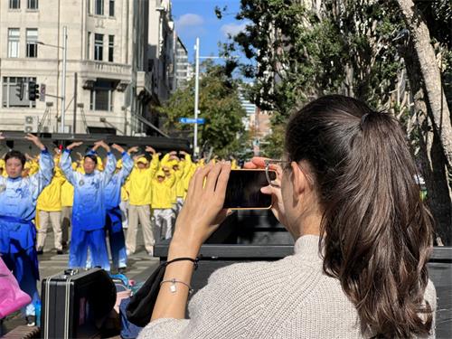 '图4:法轮功学员集体炼功的场面祥和,吸引路人拿出手机拍照。'