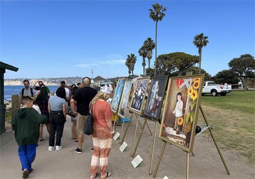 '图4:二零二二年五月七日,圣地亚哥学员在拉荷雅(La Jolla)海边洪法讲真相,“真善忍美展”的画作吸引游人驻足观看。'