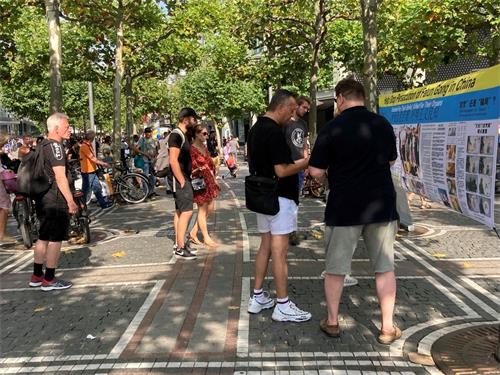 '图4:林荫道上,人们认真阅读英文横幅上的法轮功真相信息'