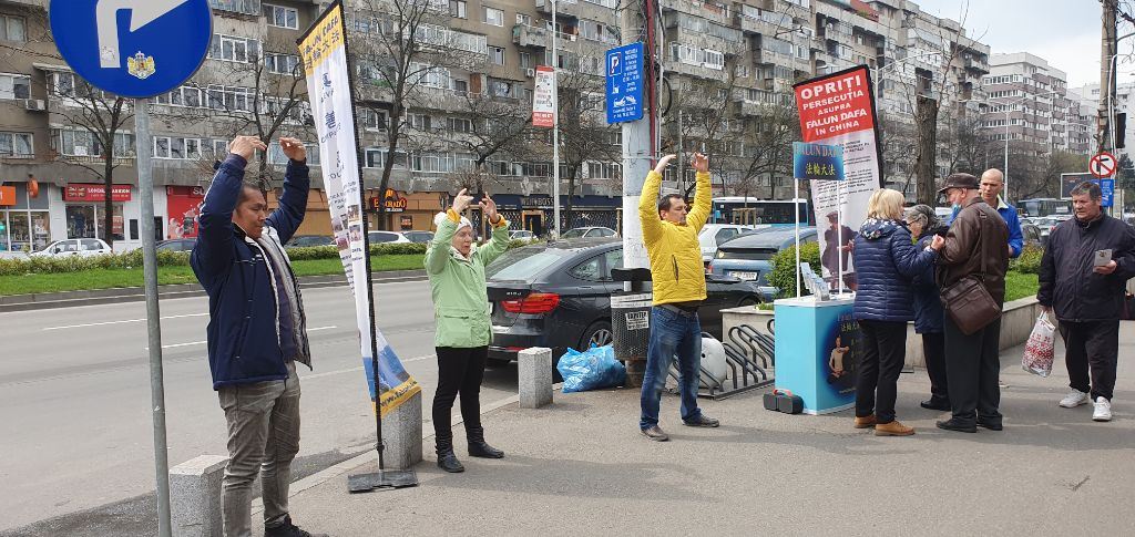 '图1:二零二三年四月八日,罗马尼亚布加勒斯特的戈尔日(Gorj)广场的法轮大法展位。三位学员在演示功法,一位学员向路人介绍大法修炼的详细情况,另一位学员在发放传单。'