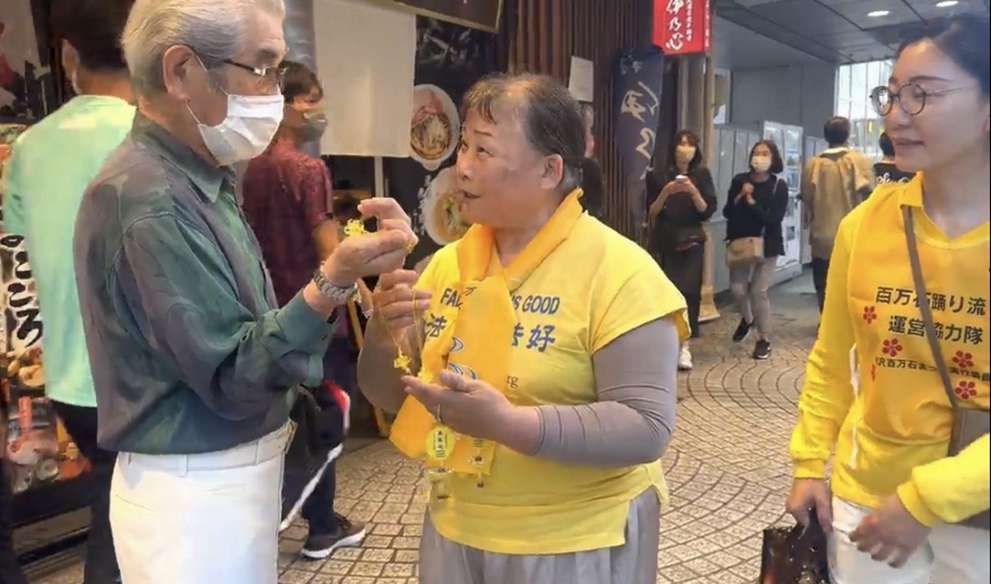 图2:法轮功学员向日本老人发放小莲花,并向观众讲述法轮大法弘传世界多个国家的美好。