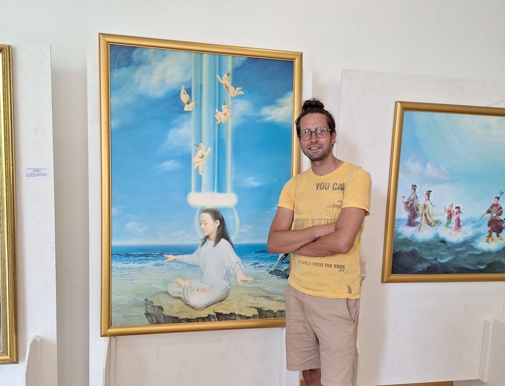 '图2:一位画展参观者在他最喜欢的画作 《天人合一》前留影。他在留言簿上写道:“在这里,你可以忘记日常琐事”,并为能经历这样的“美好时光”表示感谢。'
