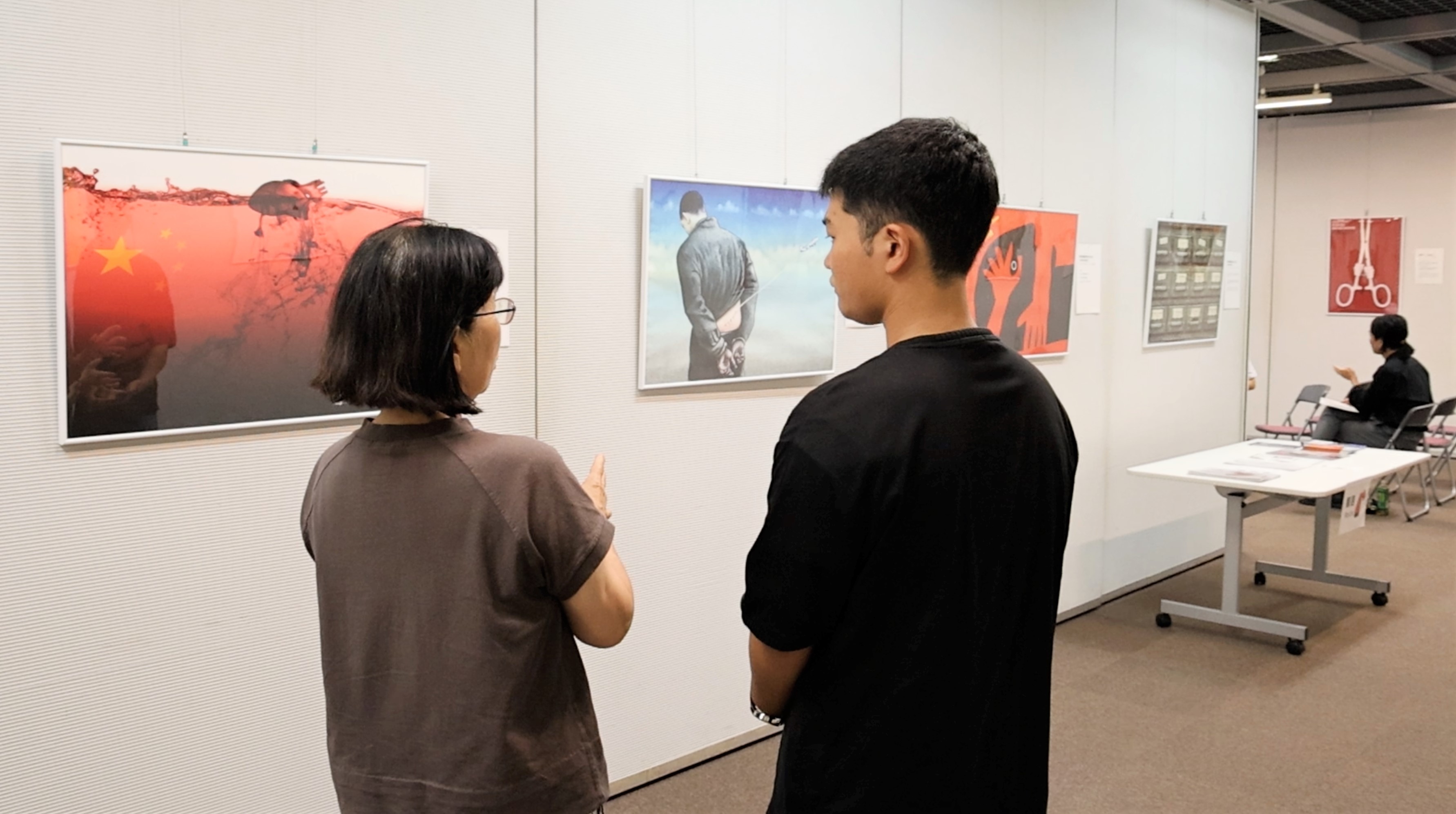 图4:大学生山岗(右)正在观看海报展并听取解说。
