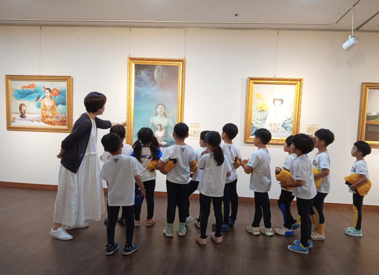 图3:组团来观看画展的YMCA(基督教青年会)的小孩们正倾听解说员的作品说明。