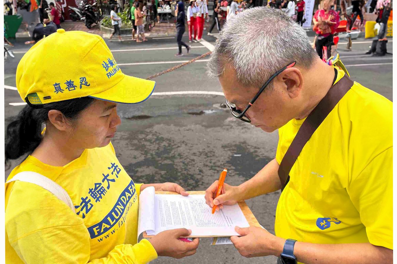 '图8:阿古斯(右)在呼吁制止活摘法轮功学员器官的请愿书上签名。'