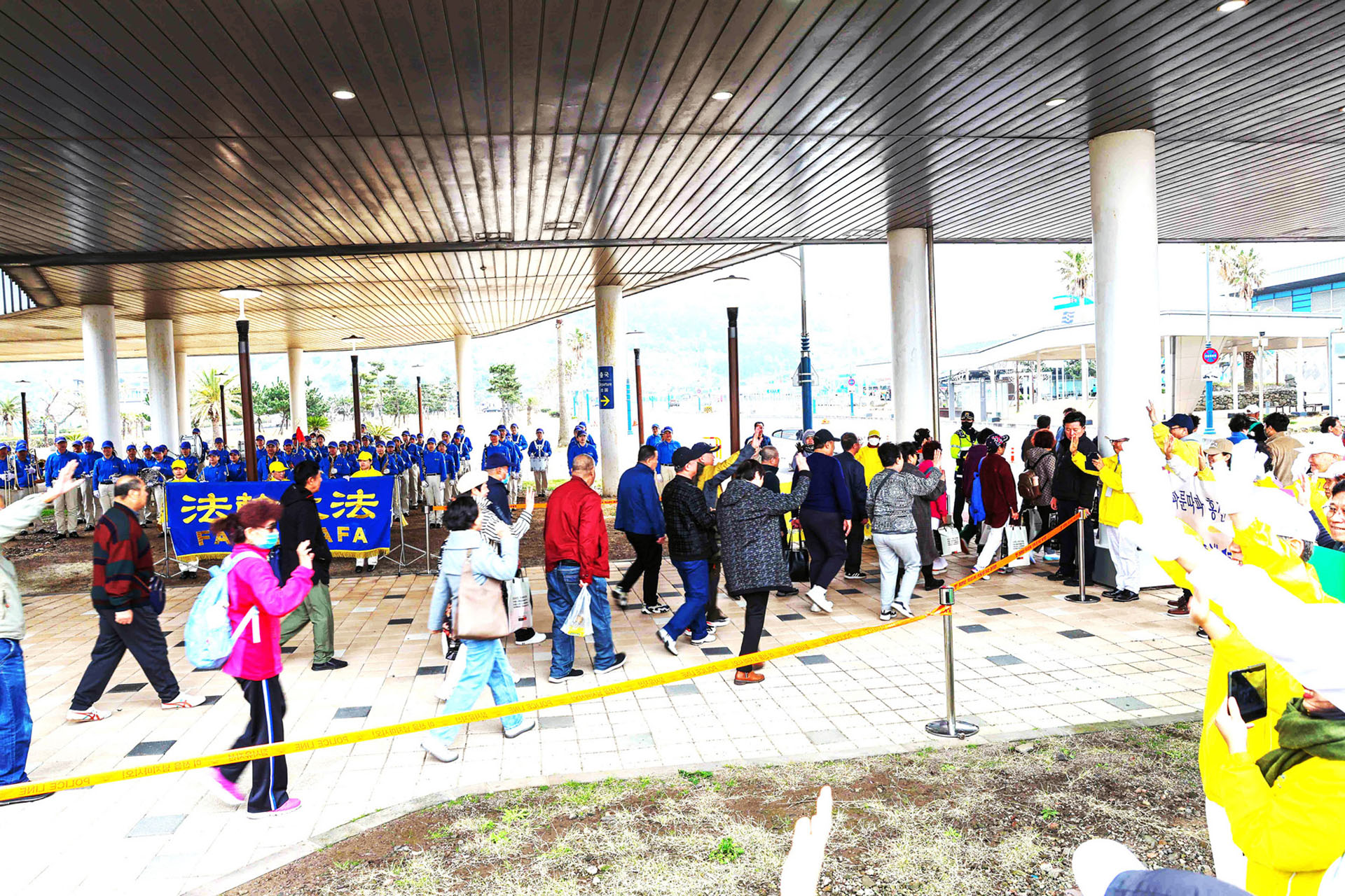 图12~13:在济州港口游客登船的路口上,学员们高举“法轮大法好”,“真善忍好”,“济州岛欢迎你”,“法轮大法洪传32周年”等横幅,展示真相给乘坐邮轮的中国游客。