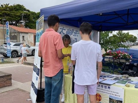 '图5:两位年轻男孩在展位上与一名法轮功学员深入交谈'