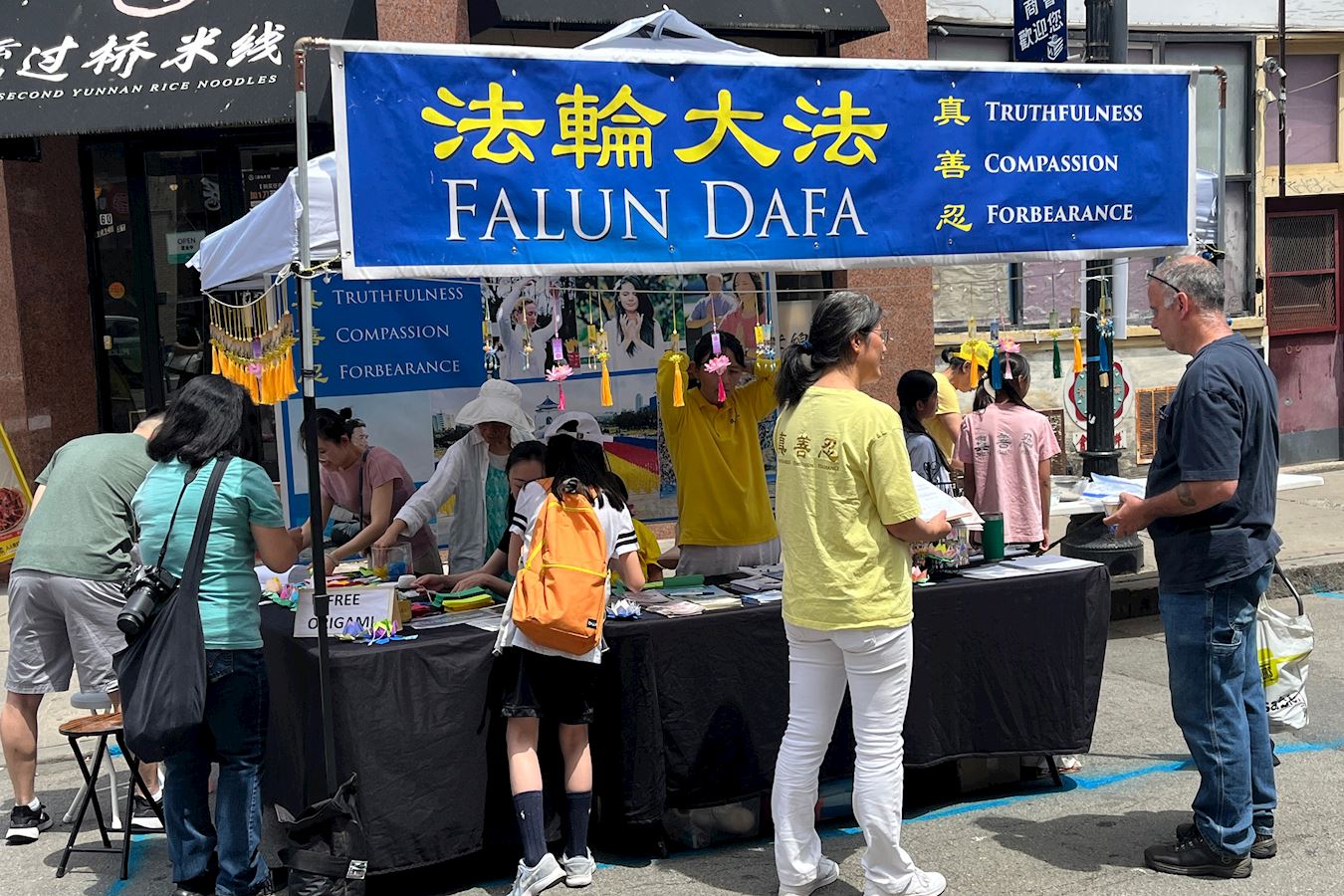 '图1:二零二五年七月五日,波士顿中国城华埠主街的夏日节庆活动。法轮功展位上参观的民众络绎不绝,有的与学员交谈了解更多法轮功的讯息。'