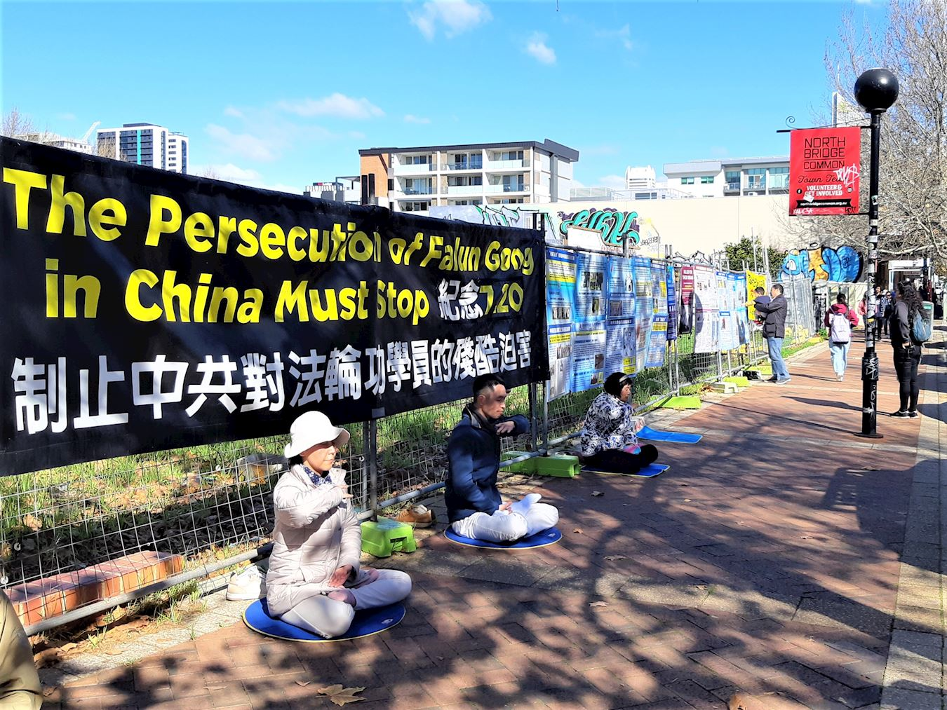 '图2~3:二零二五年七月十九日,西澳法轮功学员在珀斯北桥唐人街举办讲真相活动。图为法轮功学员在真相横幅和展板前演示功法。'
