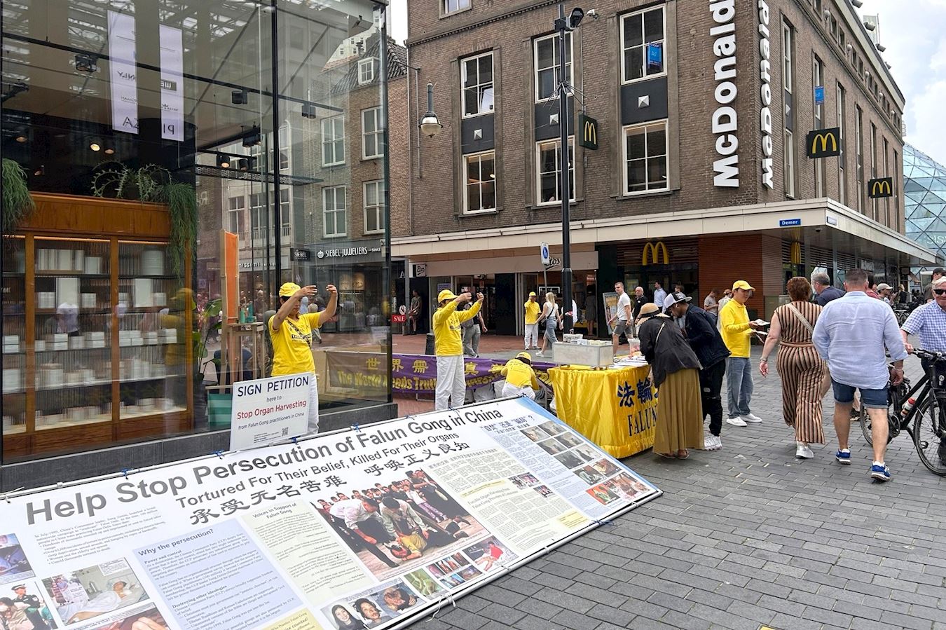 '图1~2:二零二五年七月二十六日,学员们在爱因霍温九月广场(Septemberplein)布置真相展板,讲真相。'