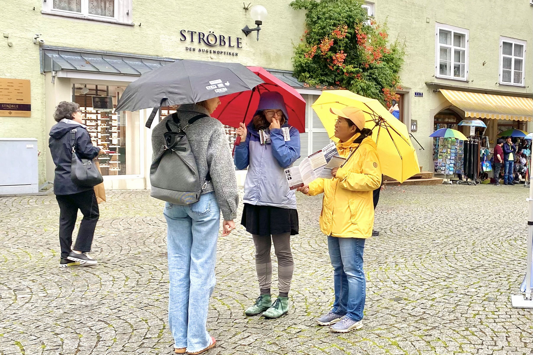 图2~4:二零二五年八月二日,法轮功学员在德国林岛(Lindau)市政厅前俾斯麦广场(Bismarck Platz)冒雨举办活动。